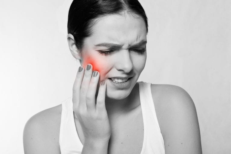 Young woman holding the side of her face portraying a dental emergency
